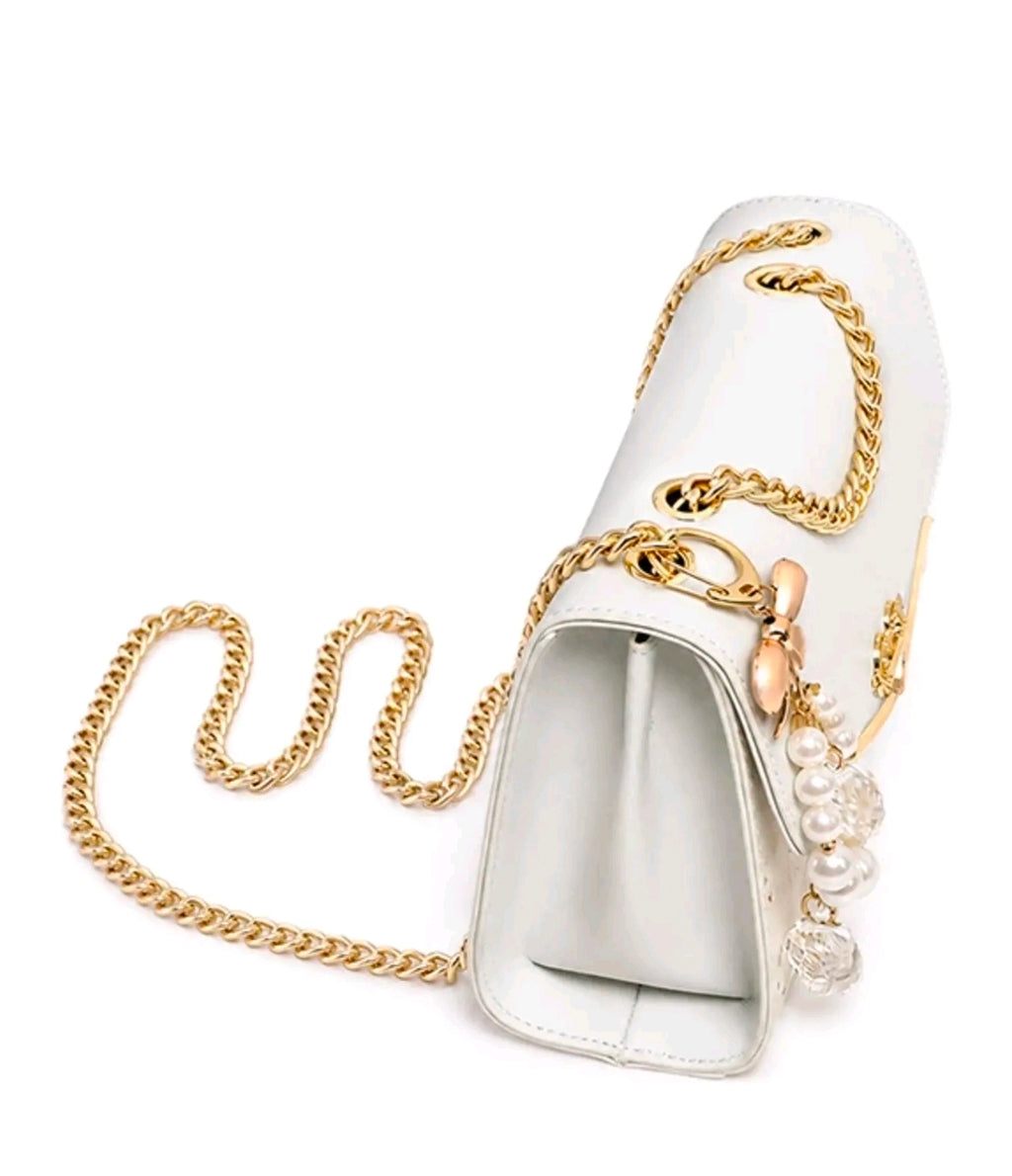 Esta cartera bandolera de diseño estructurado destaca por su estética femenina y sus detalles de fantasía con acabados metálicos en tono dorado.