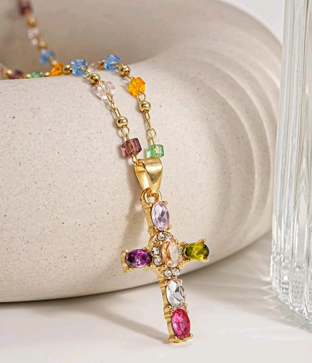 Collar con dije de cruz de piedras preciosas multicolores, un accesorio de estilo religioso y moderno que resalta por su diseño vibrante.