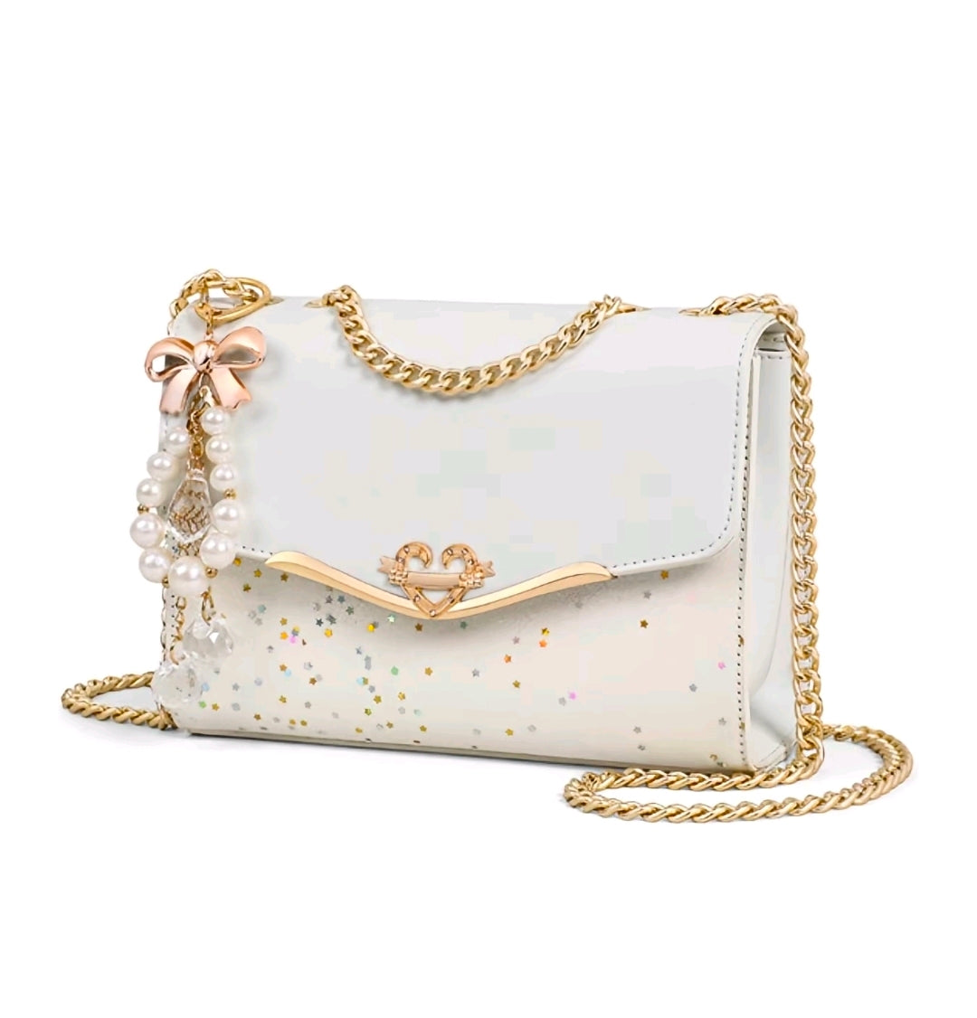 Esta cartera bandolera de diseño estructurado destaca por su estética femenina y sus detalles de fantasía con acabados metálicos en tono dorado.